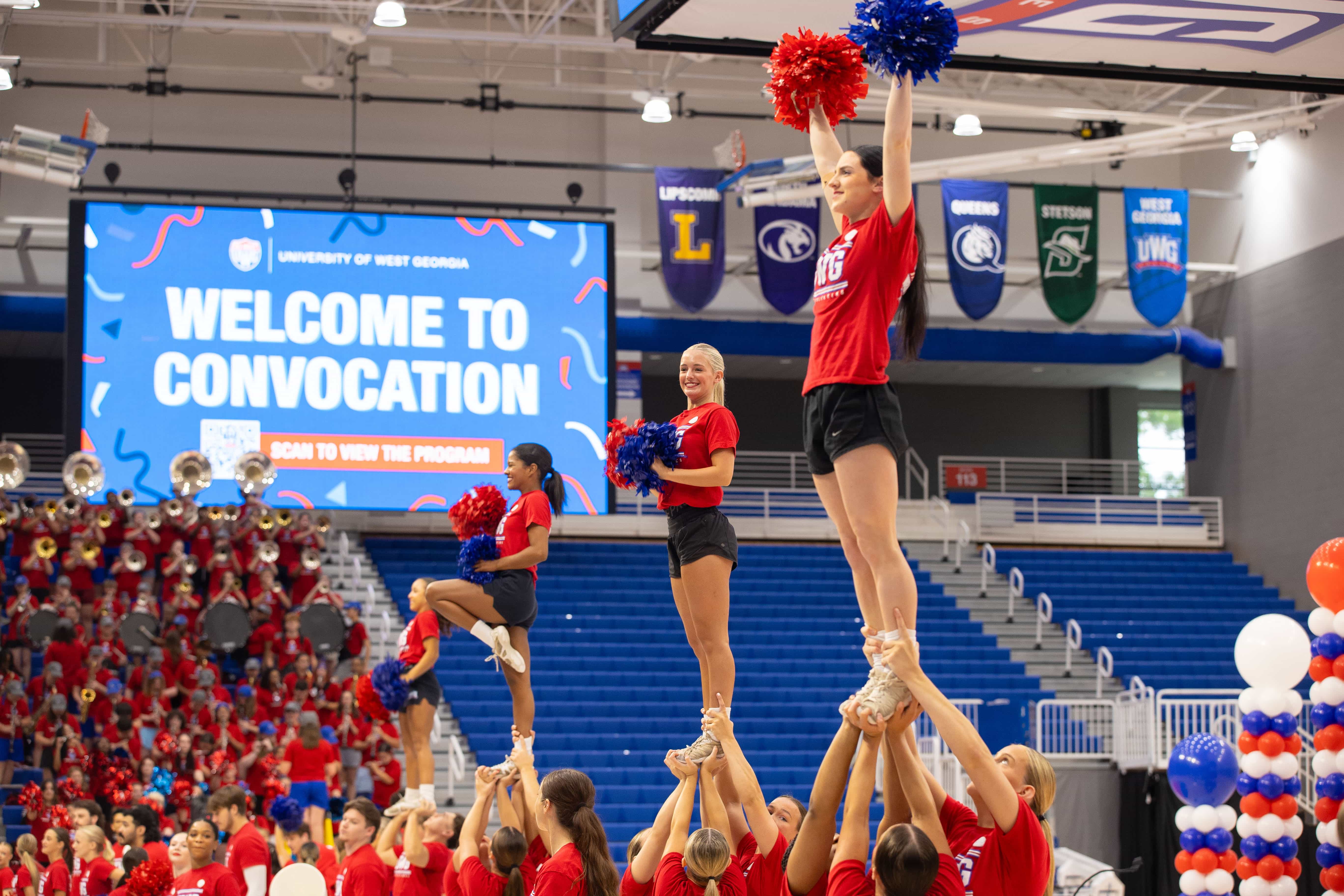 Cheerleaders on basketball court wearing red with crowd in bleachers also wearing red.