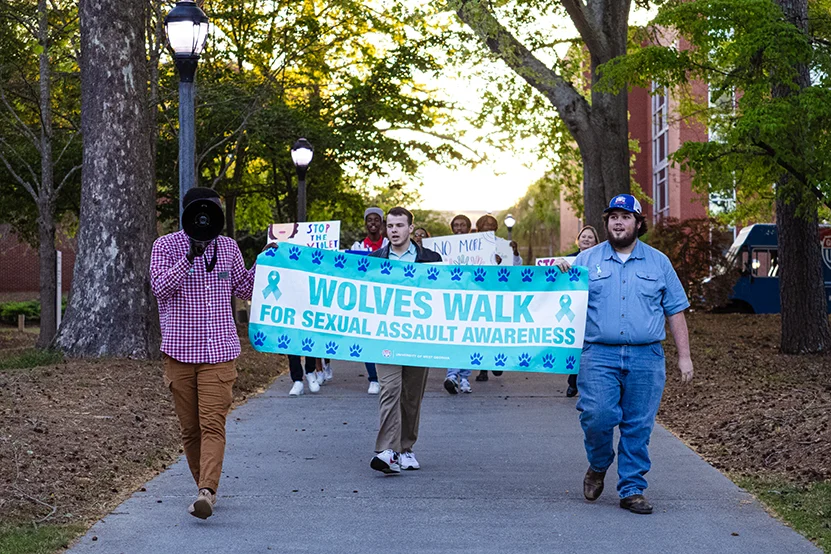 Students with a banner that says "wolves walk for sexual assault awareness"