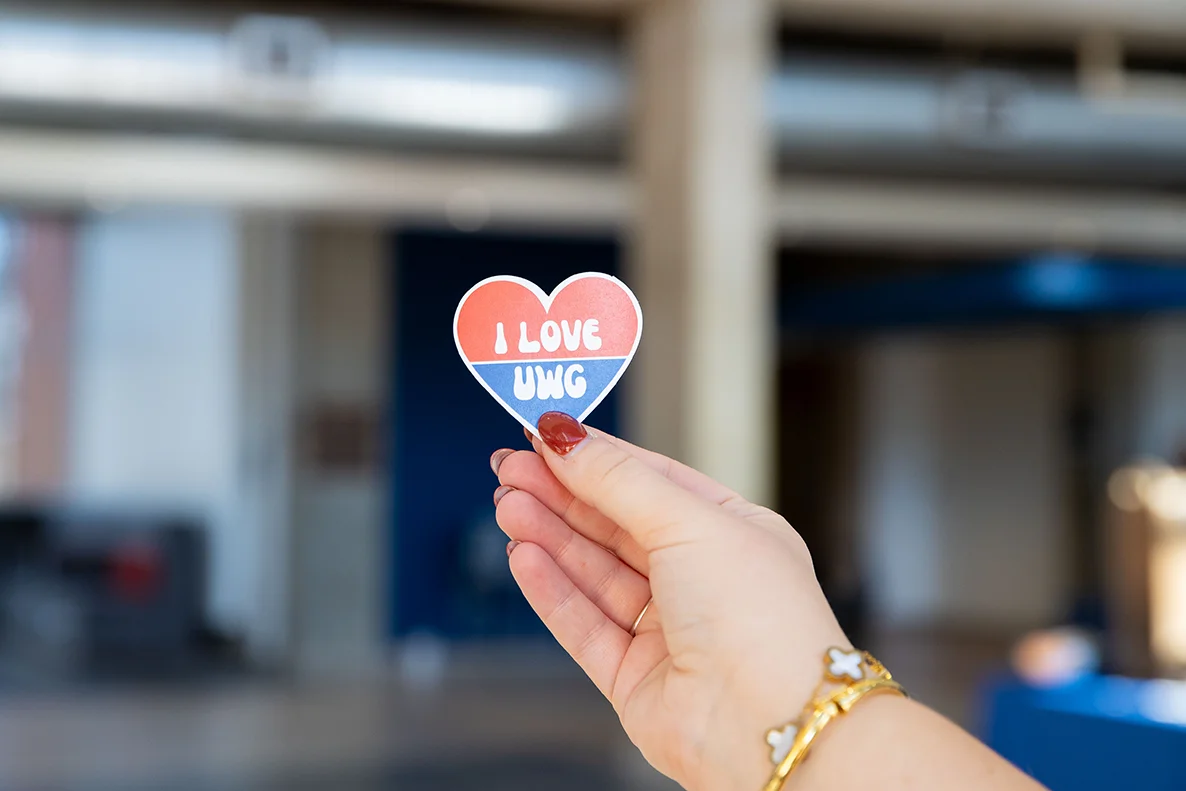 A person holding a sticker that says I love UWG