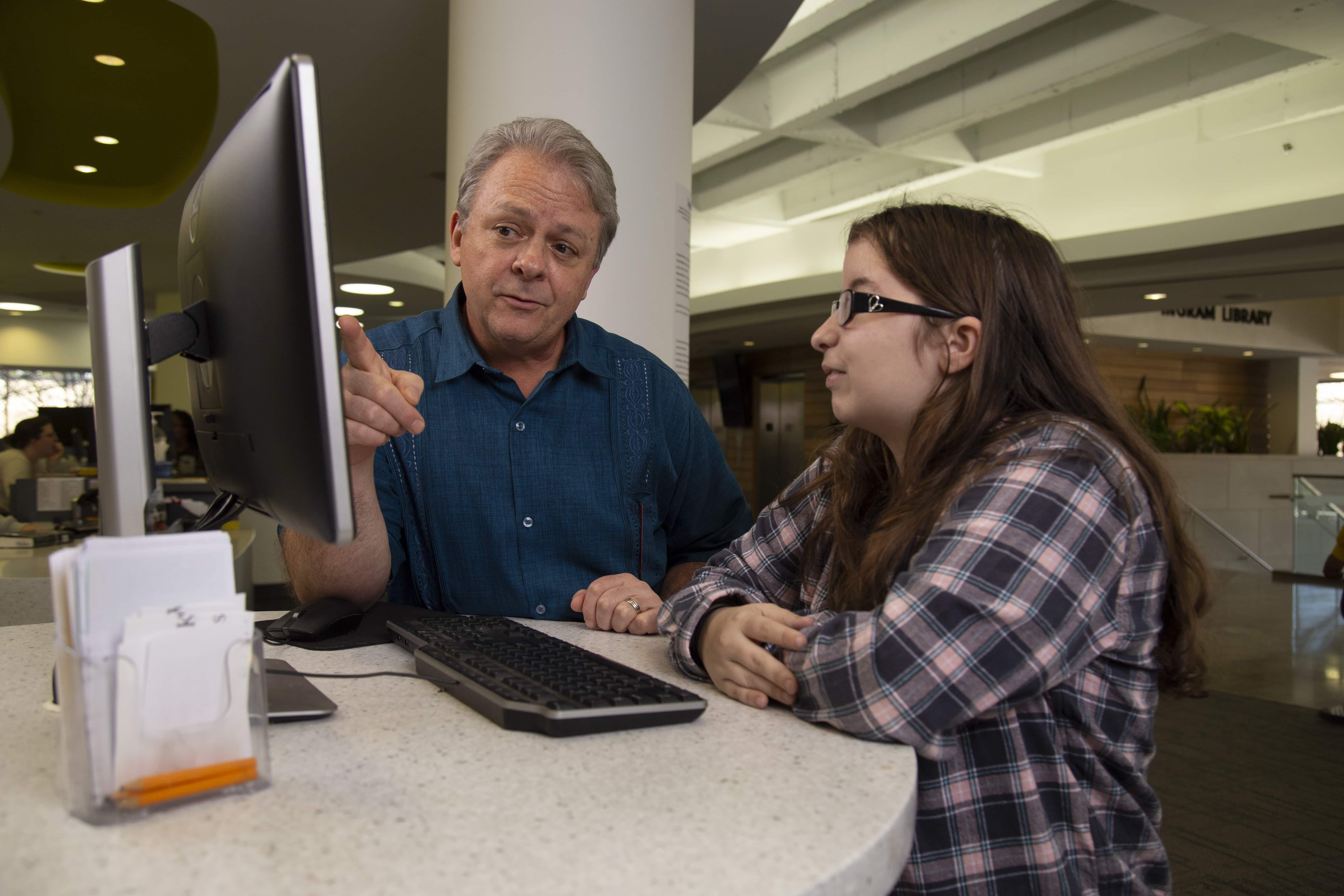 Staff member assisting a student with a computer in the library.